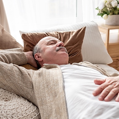 Older man sleeping on couch with one hand behind head