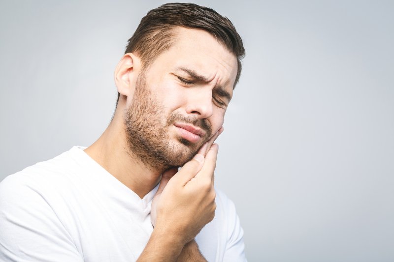 person with TMJ pain holding their cheek