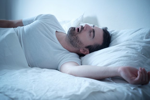 person with sleep apnea laying snoring while asleep in bed