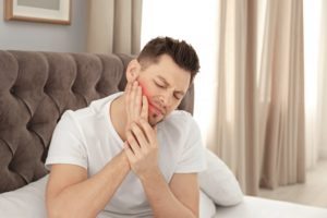 a man holding his jaw due to pain when he wakes up in the morning