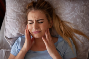 Woman lying in pain and massaging her aching jaw